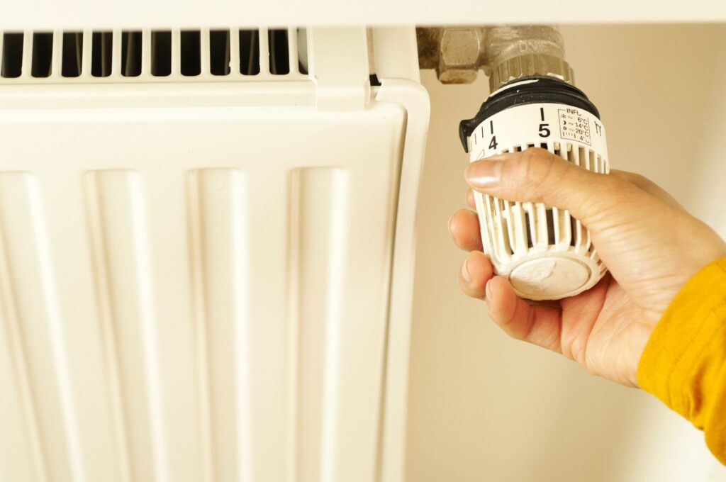 Hand dreht am Thermostat eines Heizkörpers